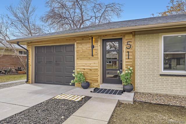 view of exterior entry featuring a garage, driveway, brick siding, and roof with shingles