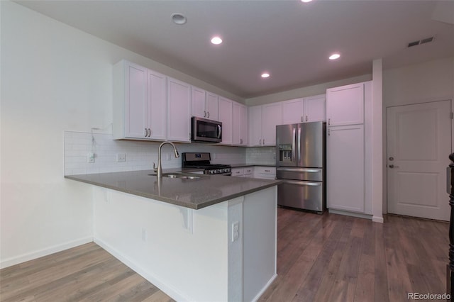 15443 W 65th Ave Unit B, Arvada, CO 80007 - kitchen featuring stainless steel appliances, a peninsula, wood finished floors, decorative backsplash, and recessed lighting