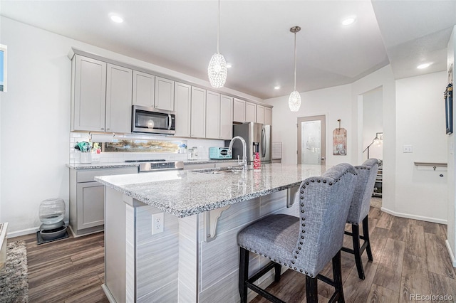 kitchen with gray cabinets, decorative light fixtures, sink, stainless steel appliances, and a center island with sink