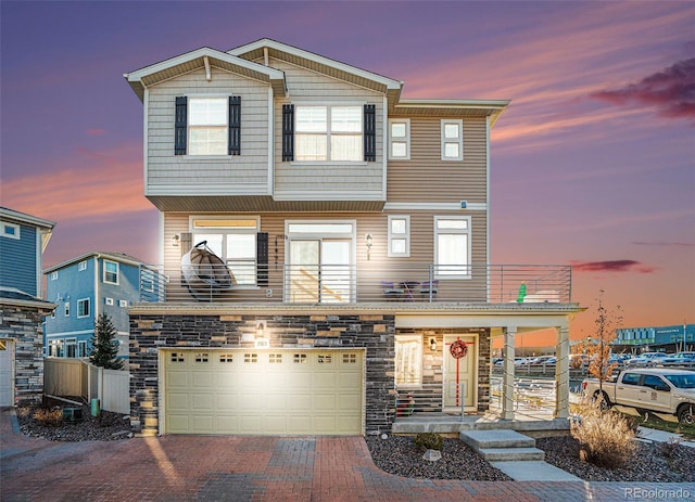 view of front of home featuring a balcony, covered porch, a garage, stone siding, and decorative driveway