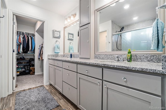 full bathroom featuring a walk in closet, a sink, wood finished floors, a shower stall, and double vanity