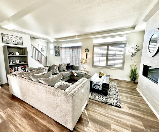 living room featuring a tray ceiling, a textured ceiling, wood finished floors, and stairs