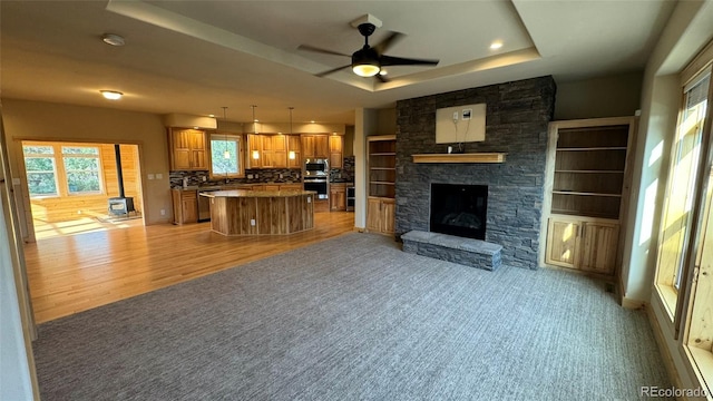 living room featuring a raised ceiling, a fireplace, ceiling fan, and light hardwood / wood-style flooring