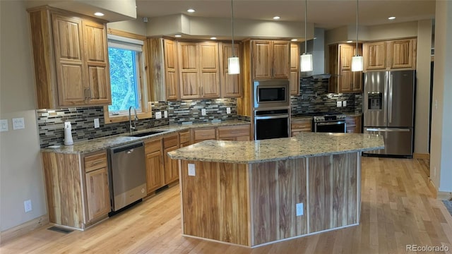 kitchen with pendant lighting, wall chimney range hood, appliances with stainless steel finishes, a center island, and light stone counters