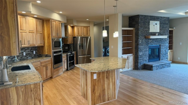 kitchen featuring pendant lighting, appliances with stainless steel finishes, a center island, light stone countertops, and washer / dryer