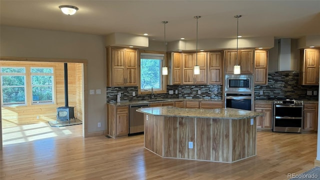 kitchen featuring appliances with stainless steel finishes, a wood stove, a center island, light stone countertops, and wall chimney range hood