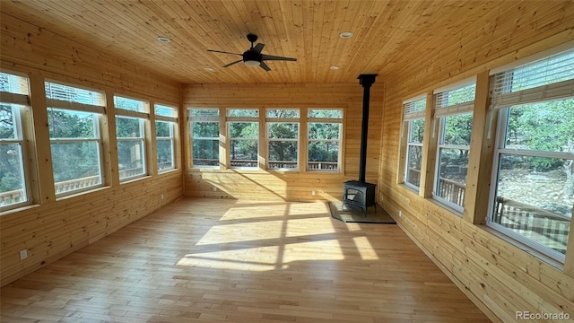 unfurnished sunroom with ceiling fan, a wood stove, and wood ceiling