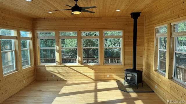 unfurnished sunroom with wood ceiling, ceiling fan, and a wood stove