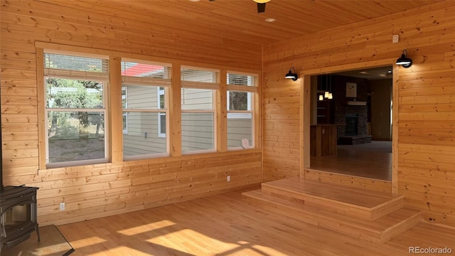 unfurnished sunroom featuring wood ceiling, ceiling fan, and a wood stove