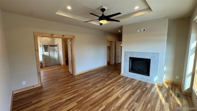 unfurnished living room featuring dark hardwood / wood-style floors, ceiling fan, and a tray ceiling