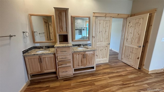 bathroom with a sink, baseboards, wood finished floors, and two vanities