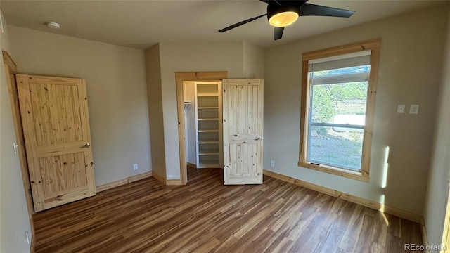 unfurnished bedroom with a spacious closet, dark wood-type flooring, a closet, and ceiling fan