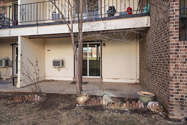 rear view of property featuring a balcony, a wall unit AC, stucco siding, a patio area, and brick siding