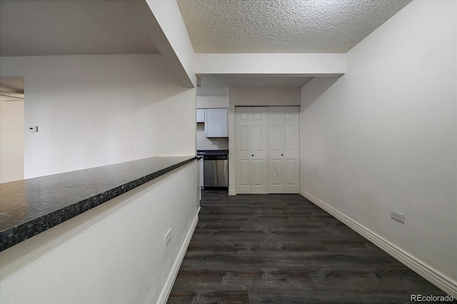 hallway featuring a textured ceiling, dark wood-type flooring, and baseboards