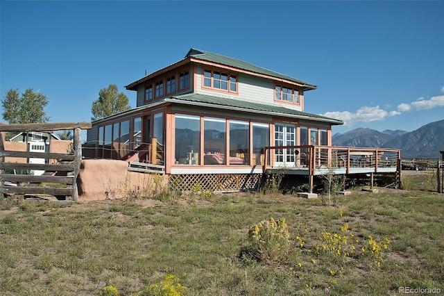 back of house featuring a deck with mountain view, a yard, and a sunroom