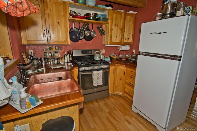 kitchen featuring white fridge, stainless steel range with gas stovetop, light hardwood / wood-style floors, and sink