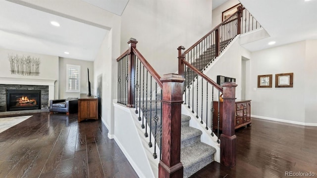 stairs featuring a stone fireplace, wood-type flooring, and a high ceiling