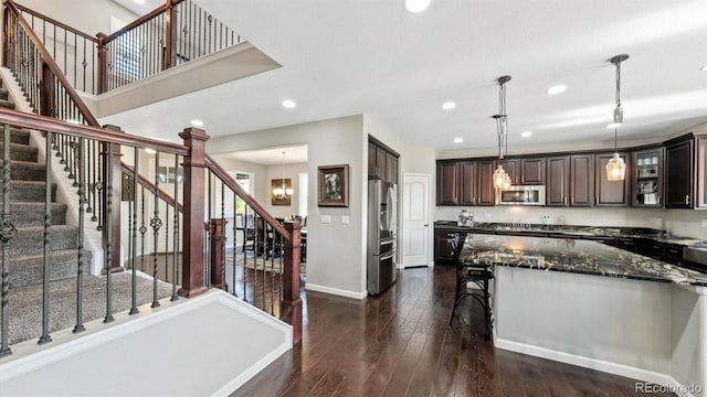 kitchen featuring appliances with stainless steel finishes, decorative light fixtures, dark stone countertops, dark hardwood / wood-style flooring, and dark brown cabinets