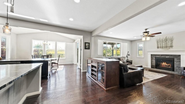 living room featuring ceiling fan, plenty of natural light, a stone fireplace, and dark hardwood / wood-style flooring