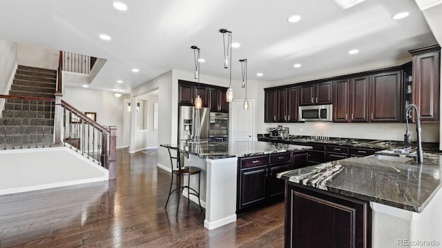 kitchen featuring sink, dark stone countertops, stainless steel appliances, a center island, and decorative light fixtures