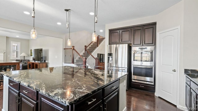 kitchen with pendant lighting, stainless steel appliances, a kitchen island, and dark stone countertops