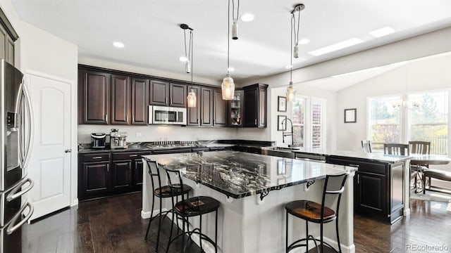 kitchen featuring decorative light fixtures, dark stone countertops, dark hardwood / wood-style floors, a kitchen island, and stainless steel appliances