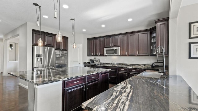 kitchen with a spacious island, stainless steel appliances, decorative light fixtures, and dark stone countertops