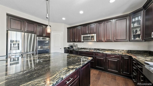 kitchen featuring appliances with stainless steel finishes, dark hardwood / wood-style floors, dark stone countertops, hanging light fixtures, and dark brown cabinets