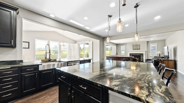 kitchen with sink, dark wood-type flooring, dark stone countertops, hanging light fixtures, and stainless steel dishwasher