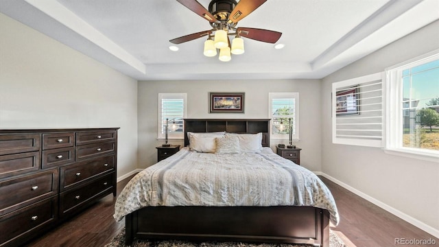 bedroom featuring dark wood-type flooring, a raised ceiling, and ceiling fan