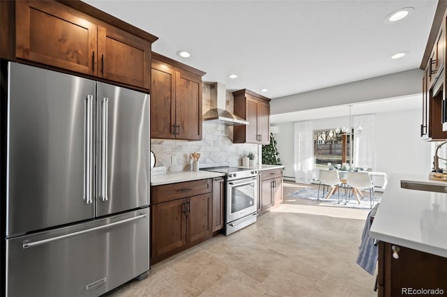 kitchen with sink, wall chimney exhaust hood, stainless steel appliances, decorative light fixtures, and decorative backsplash