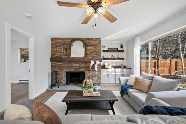 living room featuring a fireplace, a healthy amount of sunlight, light wood-type flooring, and a baseboard heating unit