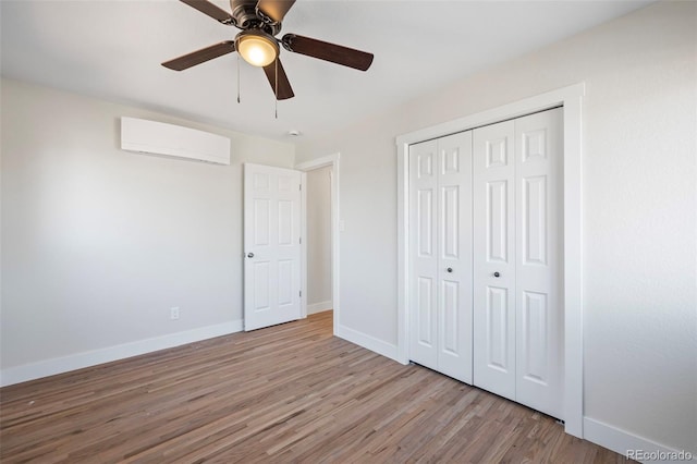 unfurnished bedroom featuring light wood-type flooring, a closet, a wall unit AC, and ceiling fan