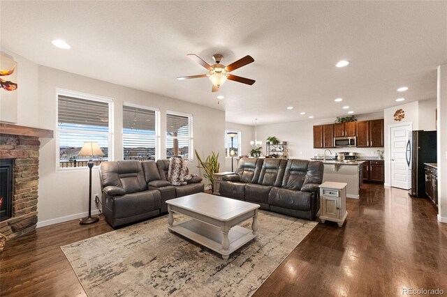 living room featuring ceiling fan, dark hardwood / wood-style floors, a stone fireplace, and sink