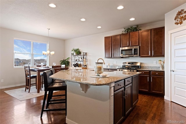 kitchen featuring pendant lighting, dark wood-type flooring, an inviting chandelier, a center island with sink, and stainless steel appliances