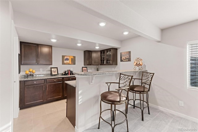 kitchen with a kitchen bar, kitchen peninsula, light stone countertops, and dark brown cabinetry