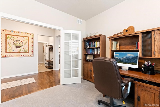 carpeted home office with french doors and vaulted ceiling