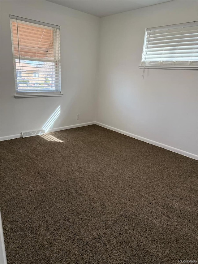 spare room featuring baseboards, dark carpet, and a healthy amount of sunlight