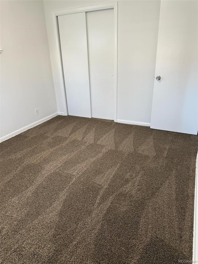 unfurnished bedroom with baseboards, a closet, and dark carpet