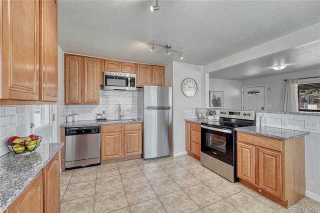 kitchen featuring light stone counters, a peninsula, a sink, stainless steel appliances, and tasteful backsplash