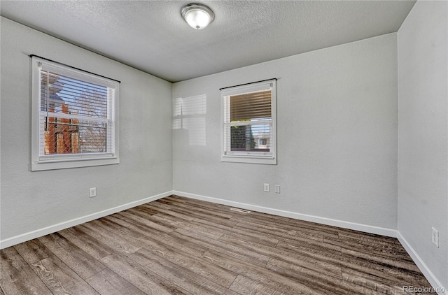 empty room with baseboards, a textured ceiling, wood finished floors, and a textured wall