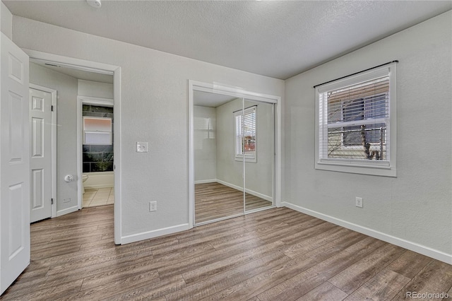 unfurnished bedroom with a textured ceiling, wood finished floors, a closet, baseboards, and a textured wall