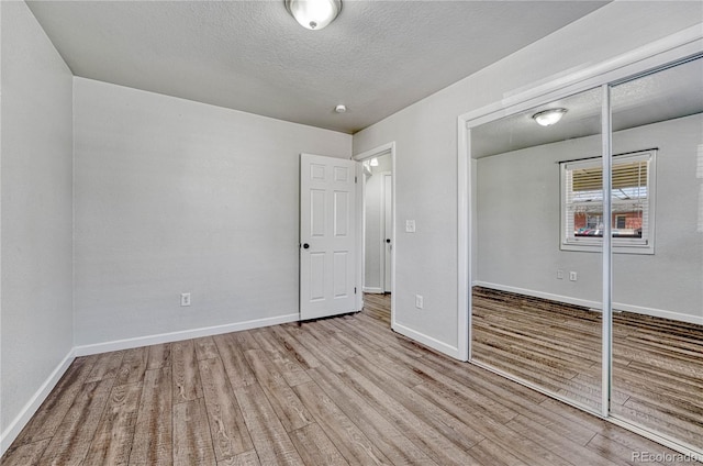 unfurnished bedroom with a textured ceiling, wood finished floors, a closet, and baseboards