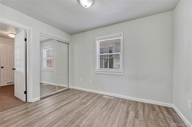 unfurnished bedroom featuring light wood finished floors, visible vents, baseboards, a closet, and a textured ceiling