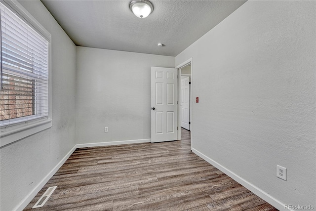 empty room with visible vents, baseboards, wood finished floors, a textured wall, and a textured ceiling