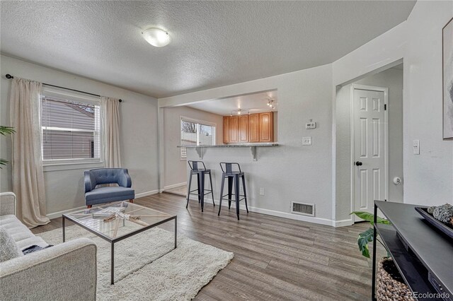 living area with a textured ceiling, baseboards, visible vents, and light wood-type flooring