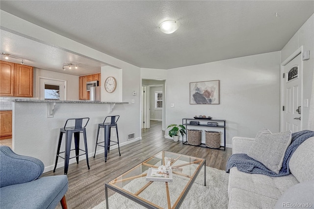 living area with baseboards, light wood-style floors, visible vents, and a textured ceiling