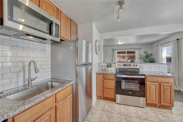 kitchen featuring a sink, stainless steel appliances, a peninsula, light tile patterned floors, and light stone countertops