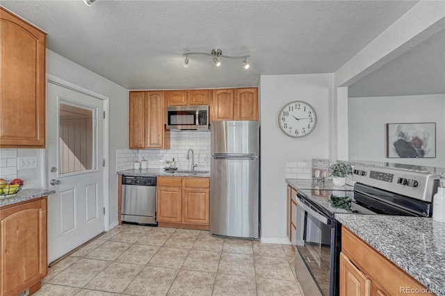 kitchen featuring tasteful backsplash, light stone countertops, light tile patterned floors, stainless steel appliances, and a sink