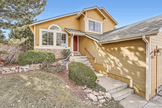 split level home featuring a shingled roof and stone siding